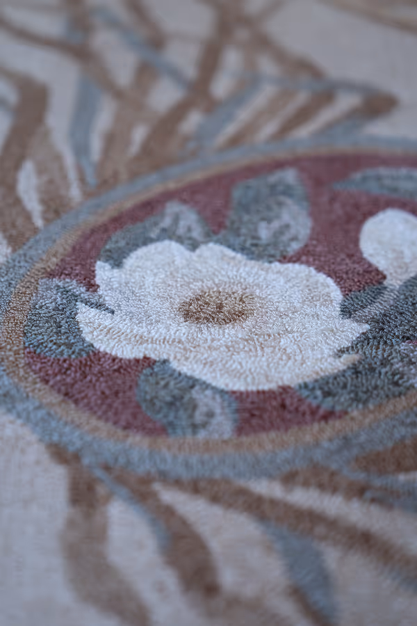 Close-up of a textured rug with a white flower and green leaves inside a red circular border.
