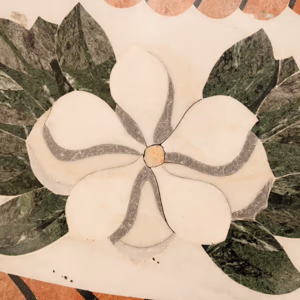 Marble inlay of a white magnolia flower with six petals and surrounding dark green leaves on a light background.