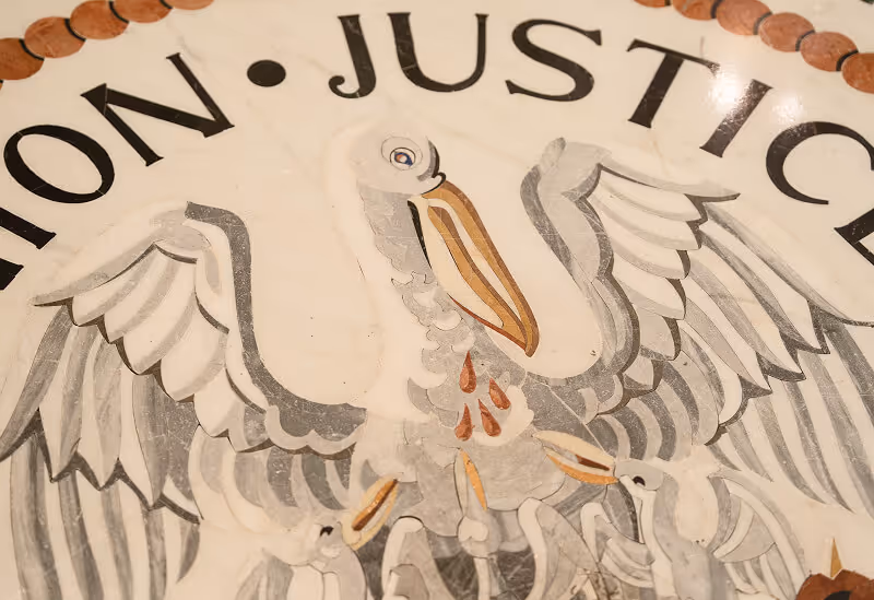 Close-up of an artistic depiction of a pelican with wings spread, feeding its young with drops of blood on its chest, under the word 'JUSTICE'.