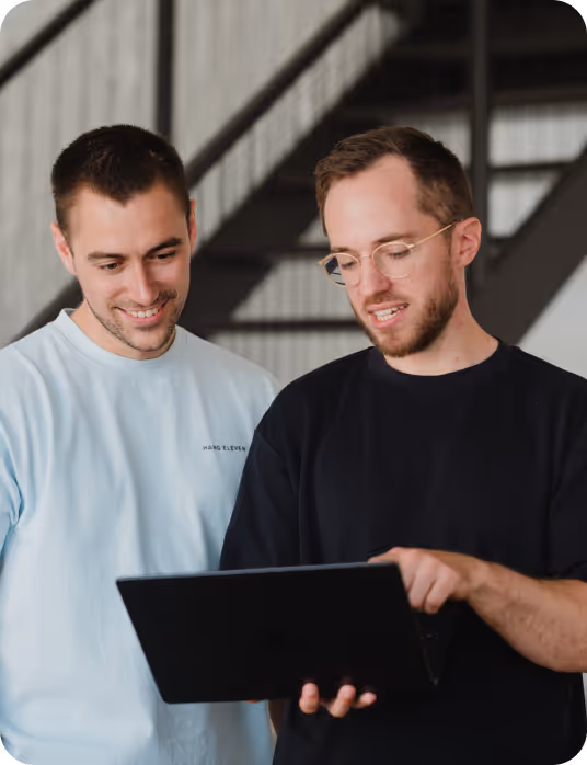 Zwei junge Männer schauen sich gemeinsam einen Laptop an, einer zeigt auf den Bildschirm.
