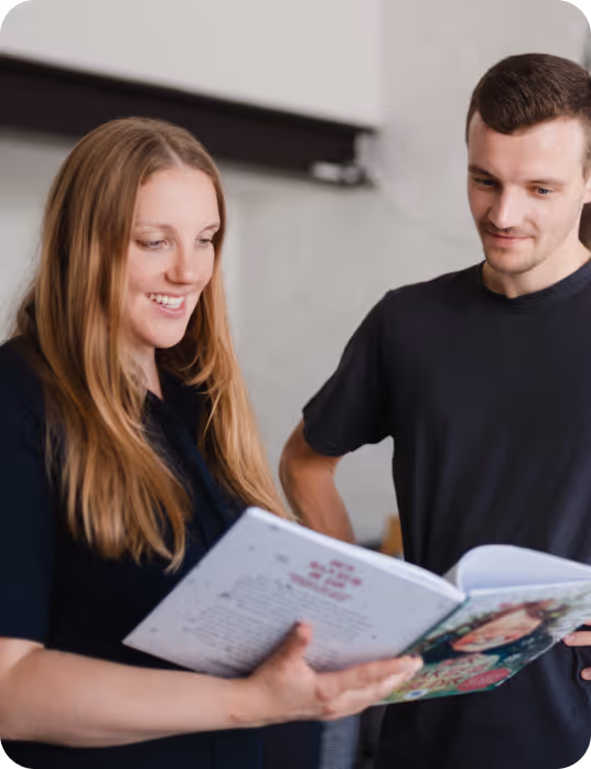 Zwei Personen, eine Frau und ein Mann, lesen gemeinsam ein Buch und lächeln.