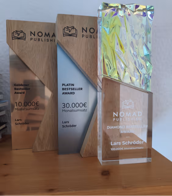 Drei Nomad Publishing Bestseller Awards aus Holz und Kristall mit Beschriftungen für 10.000€, 30.000€ und 100.000€ Monatsumsatz, vergeben an Lars Schröder.