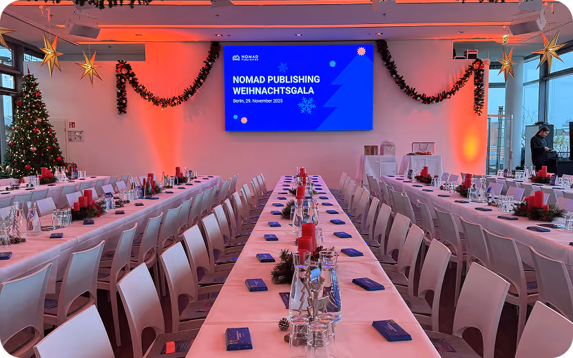 Festlich dekorierter Veranstaltungsraum mit langen, weiß gedeckten Tischen, roten Kerzen und Weihnachtsbaum, vorbereitet für die Nomad Publishing Weihnachtsgala in Berlin.