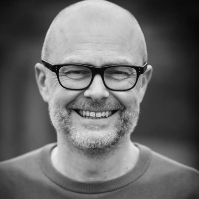 Smiling bald man with glasses and a short beard wearing a crew-neck shirt.
