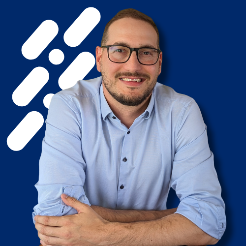 Smiling man with glasses and beard wearing a light blue shirt against a dark blue background with white graphic elements.