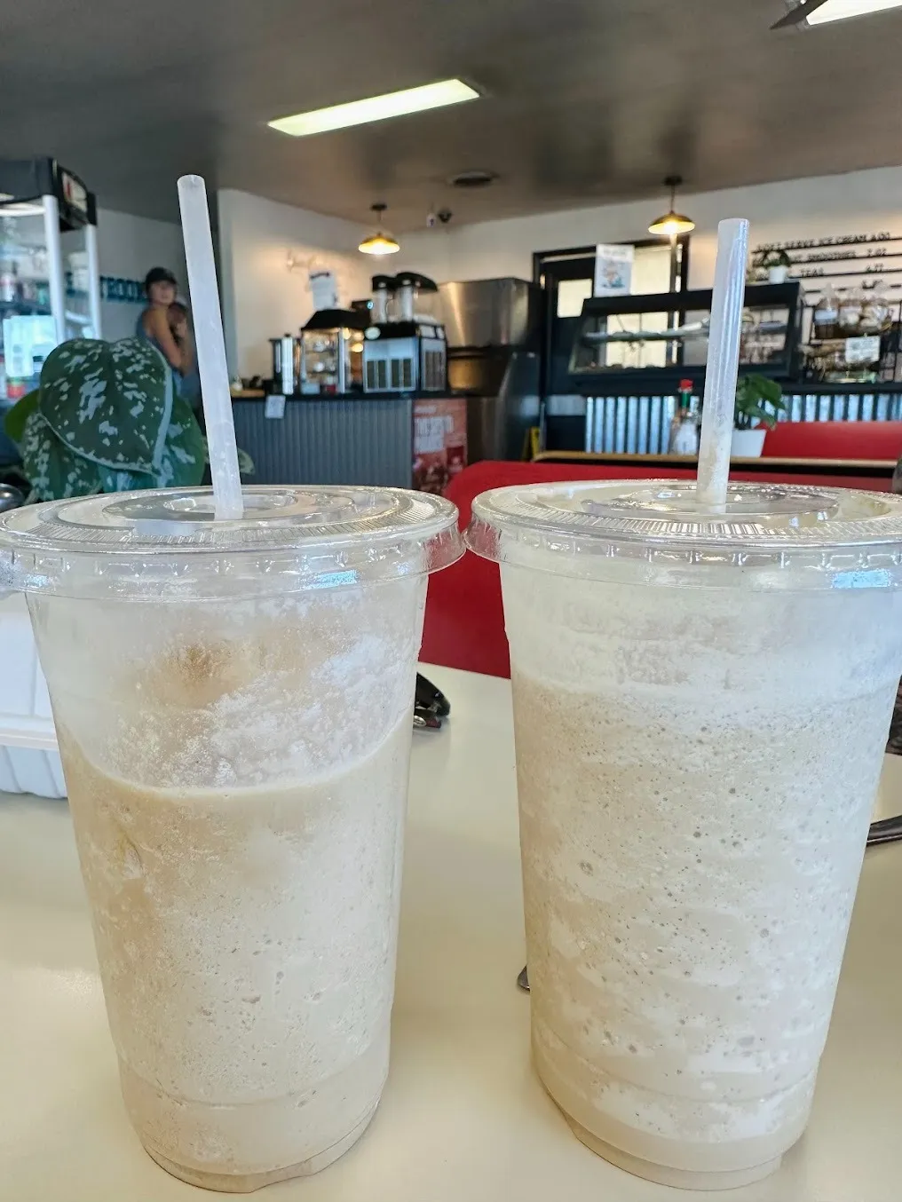 Two colorful drinks in plastic cups sit on a wooden table, with a blurred background of a casual setting.