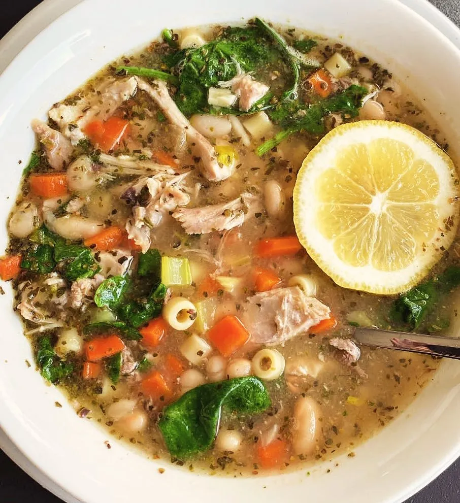 A bowl of soup filled with chicken, beans, and spinach, showcasing a hearty and nutritious meal.