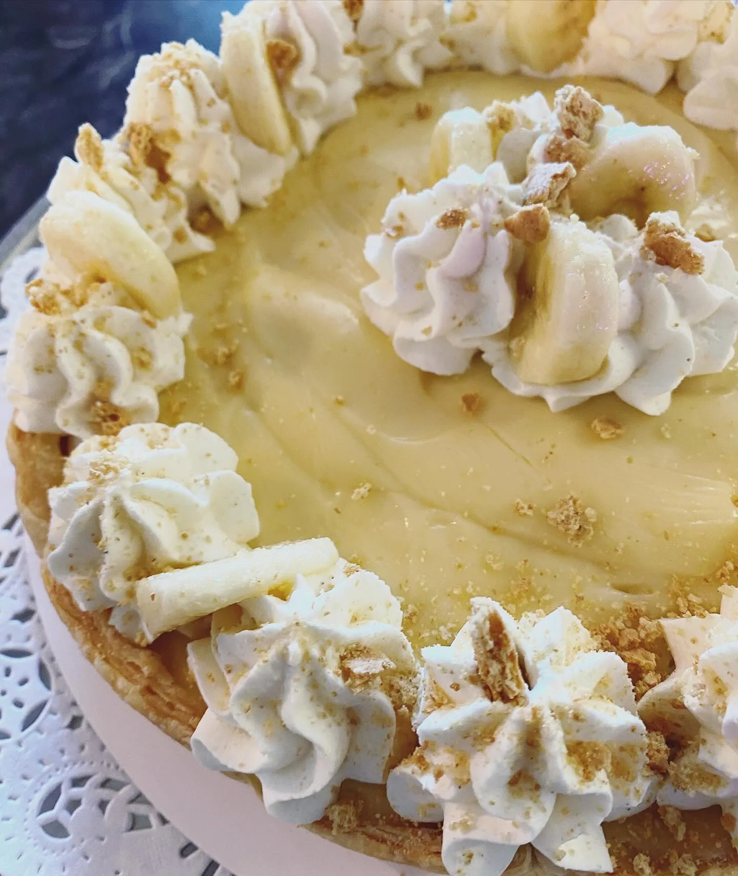 A white plate holds a delicious banana cream pie, topped with whipped cream and banana slices.
