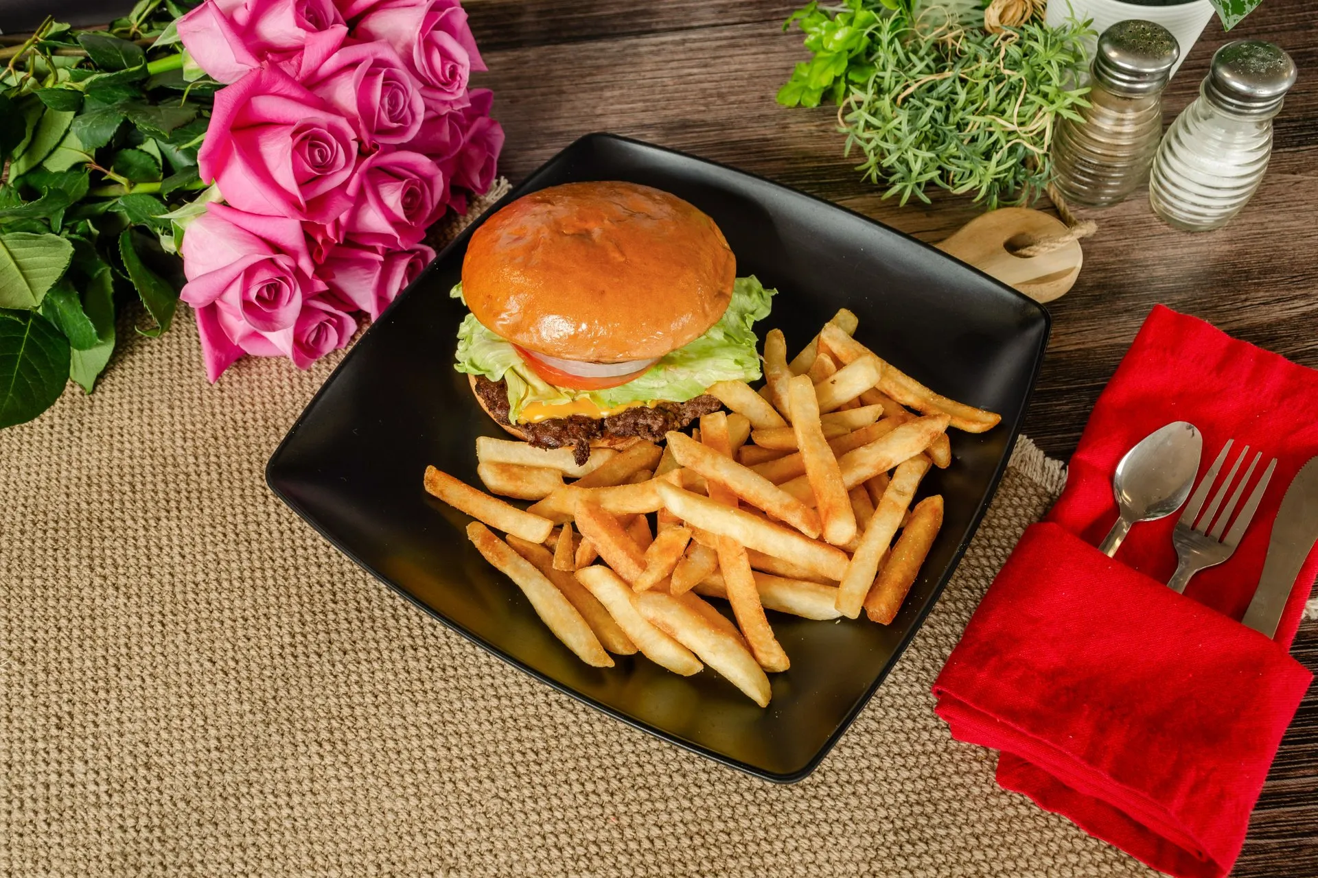 A plate with a juicy hamburger and crispy french fries sits on a rustic wooden table.