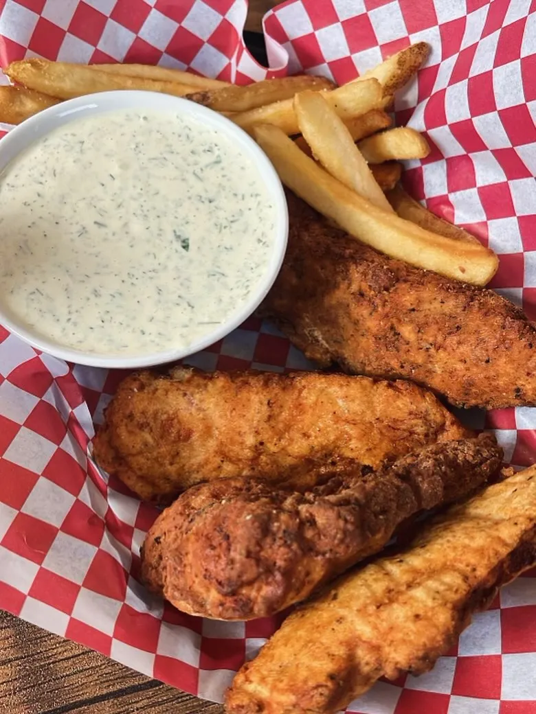 A basket filled with crispy fried chicken, golden fries, and a small container of dipping sauce.