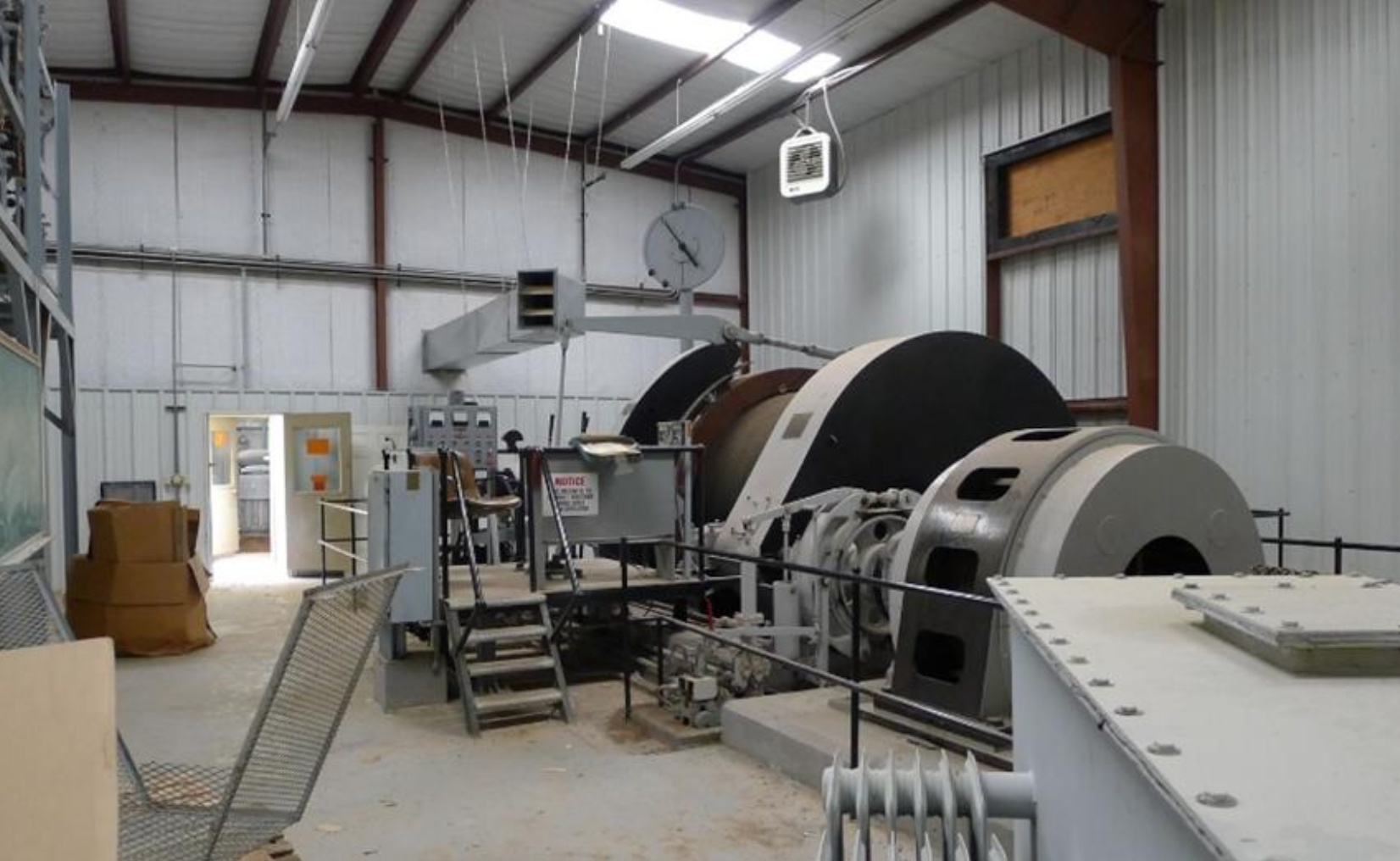 Industrial machine with large drum and control panel inside a metal-walled factory room.