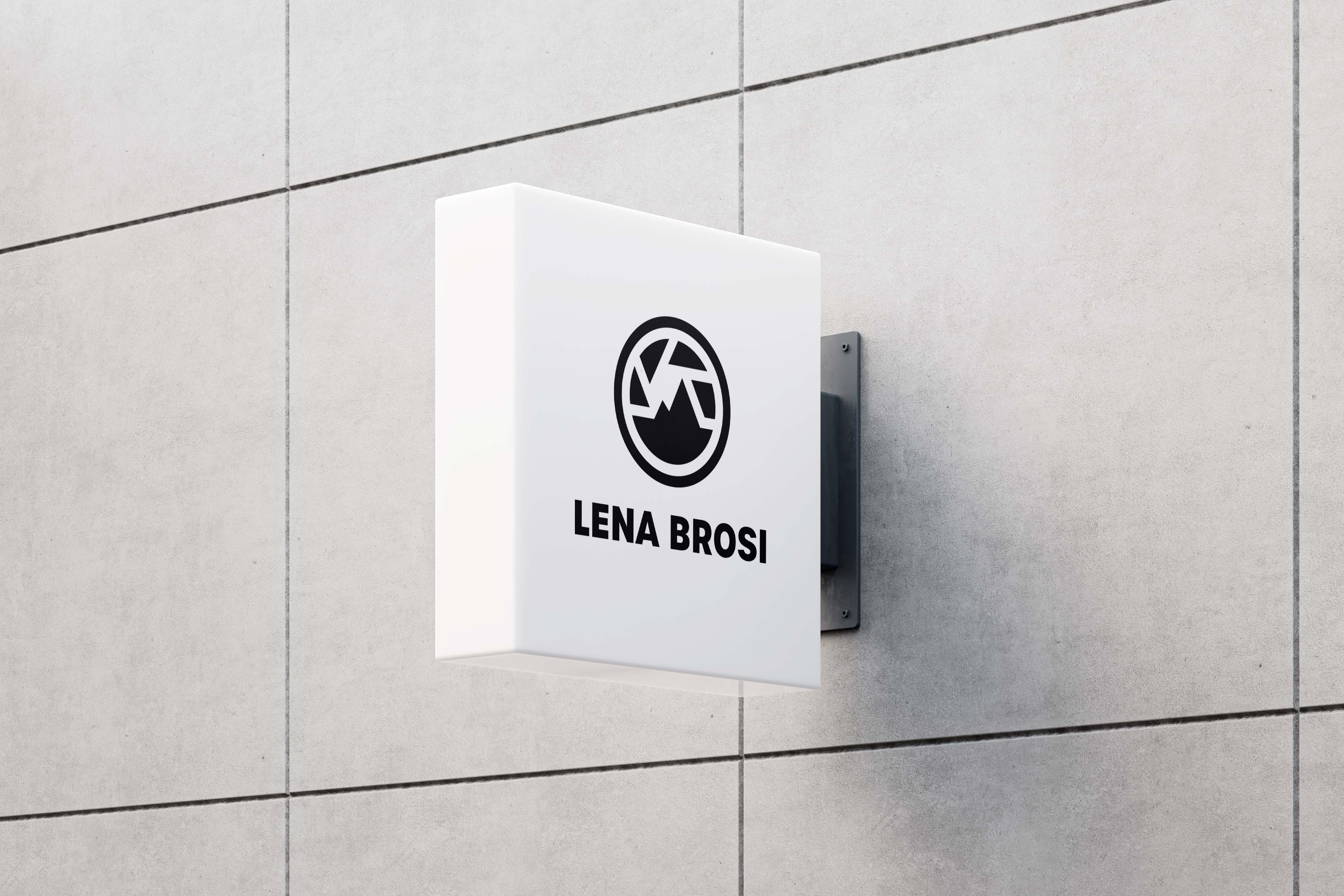 White outdoor square lightbox sign mounted on a concrete wall displaying a circular mountain logo above the text 'LENA BROSI'.