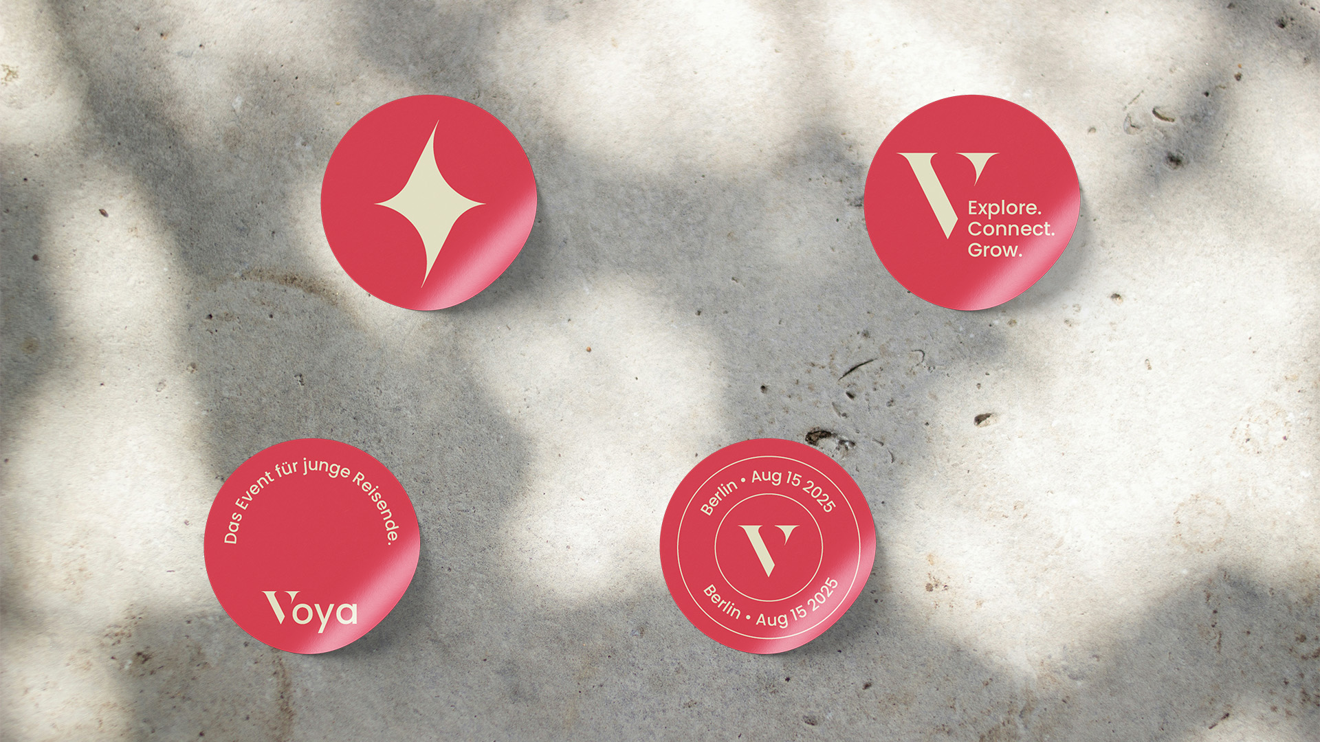 Four red circular stickers on concrete with various white logos and text including a star shape, V logo, and event details for Voya travel event in Berlin on August 15, 2025.