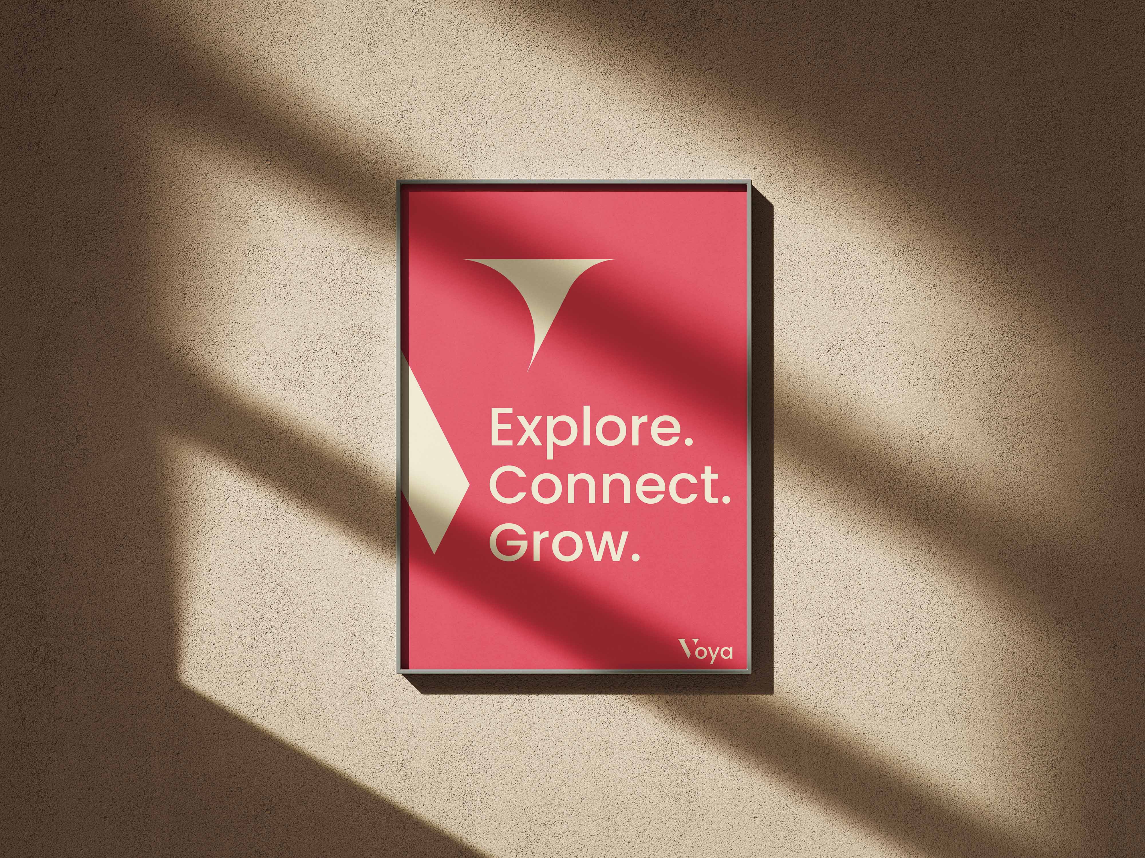 Framed red poster on a textured wall with shadows, displaying the text 'Explore. Connect. Grow.' and the Voya logo.