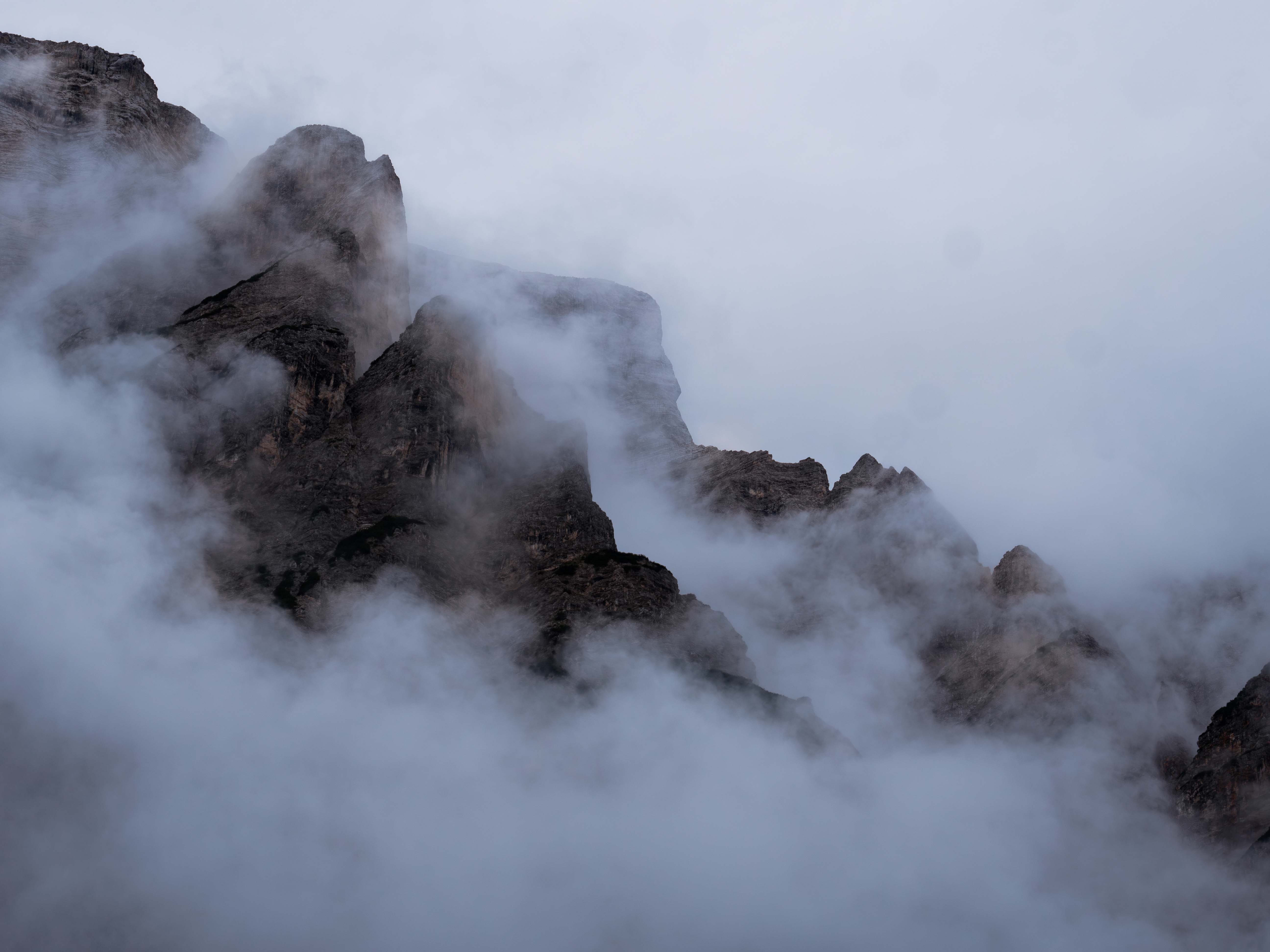 Rocky mountain peaks partially obscured by thick mist and fog under a cloudy sky.