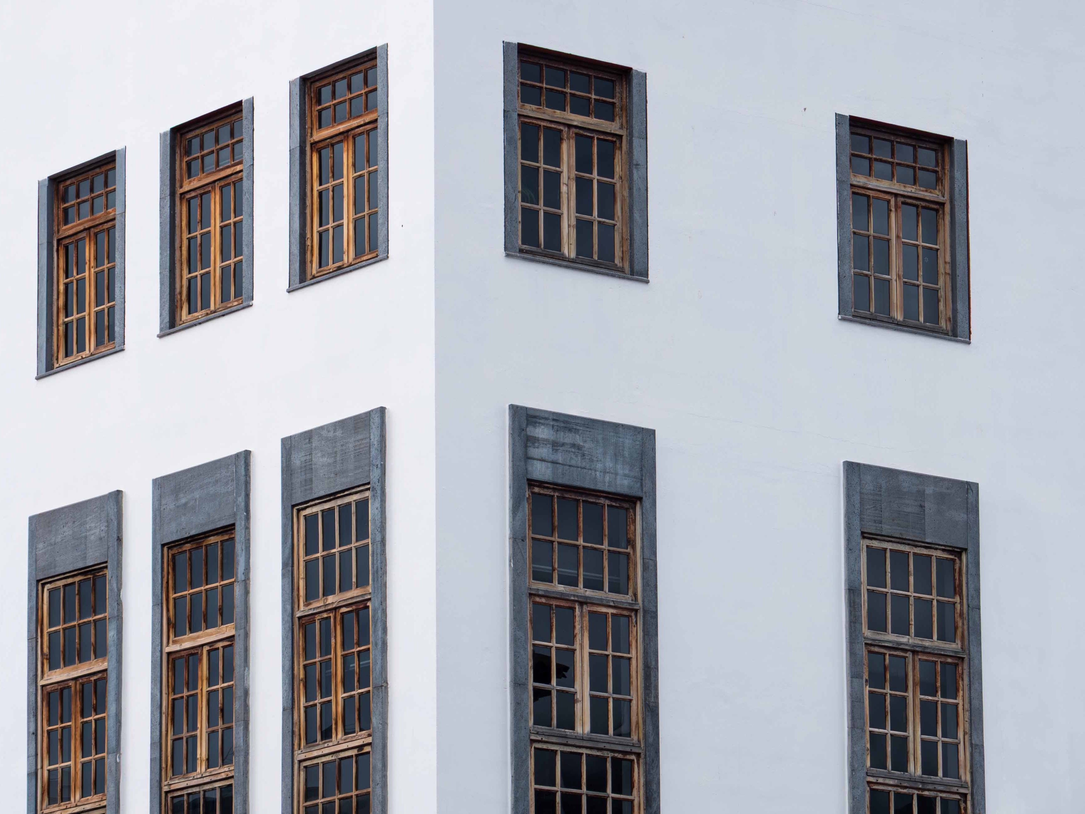 Corner of a white building with wooden-framed windows, some with gray stone borders.