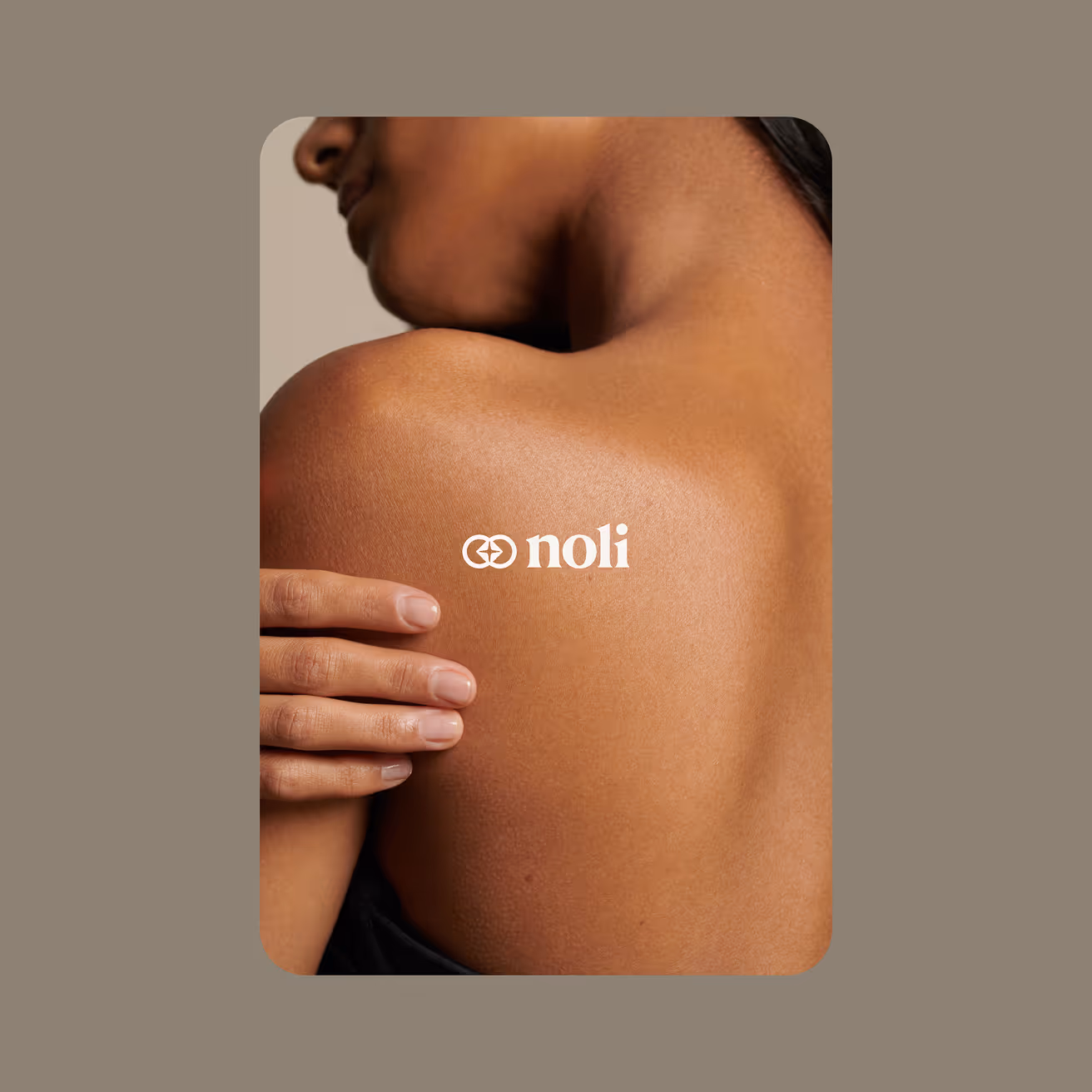 Close-up of a person with smooth brown skin touching their shoulder, with the text 'noli' centered on the shoulder.