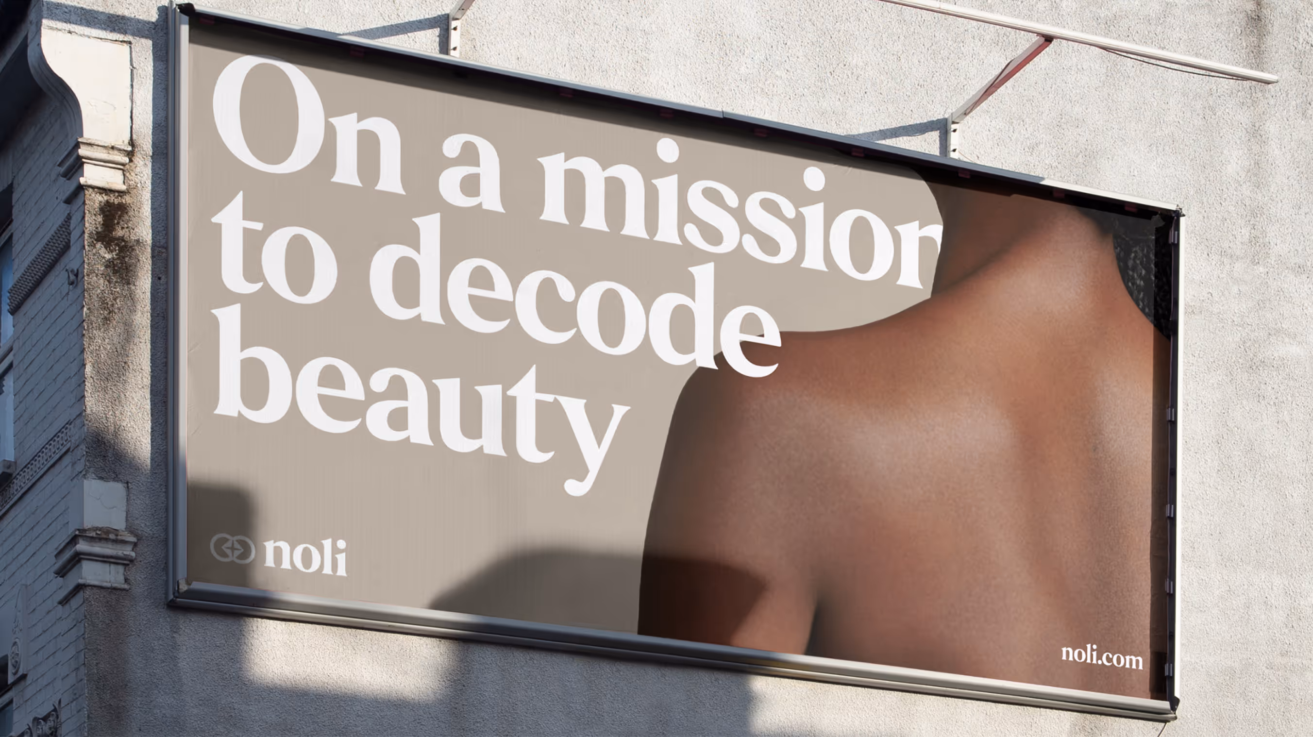 Billboard on a building wall showing the back of a bare-shouldered person with text reading 'On a mission to decode beauty' and 'noli.com'.