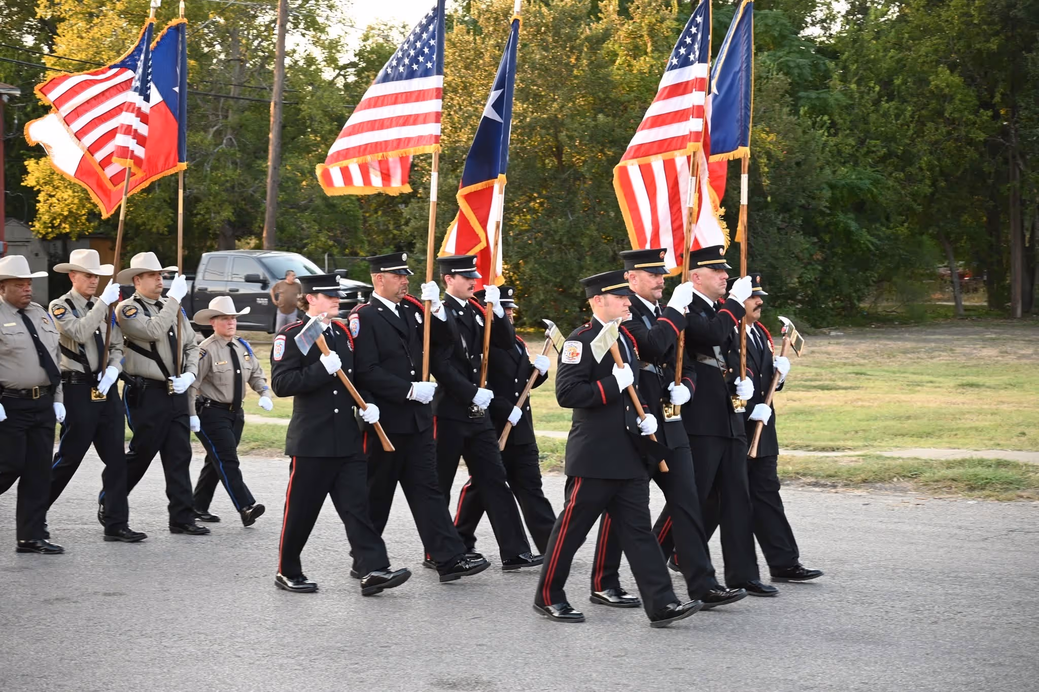 Group of uniformed officers marching in a parade holding American and Texas flags.