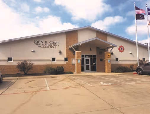 Exterior view of John H. Coats Fire Station No. 1 with two flags flying on flagpoles near the entrance.