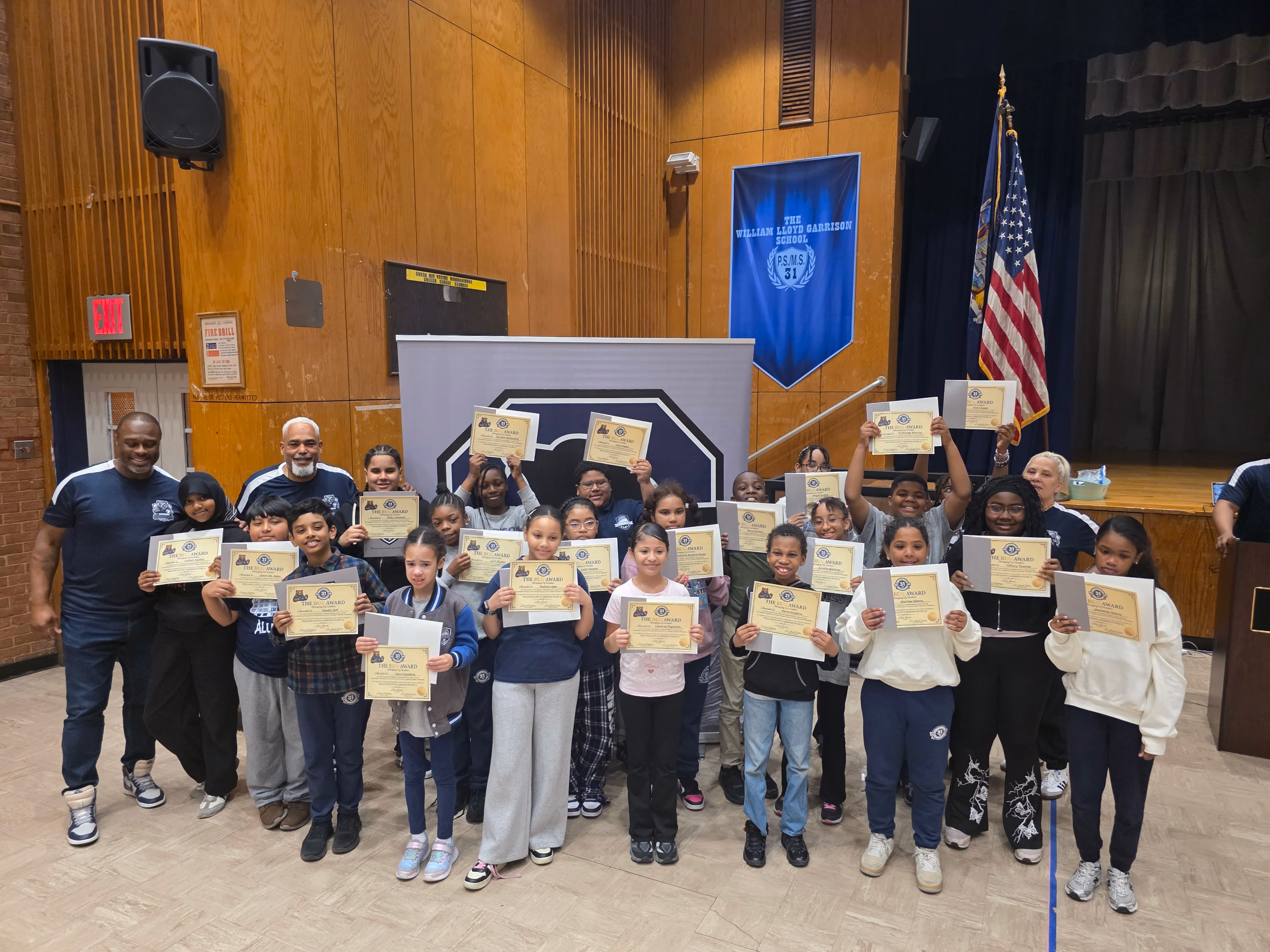 Students and staff holding award certificates in school auditorium