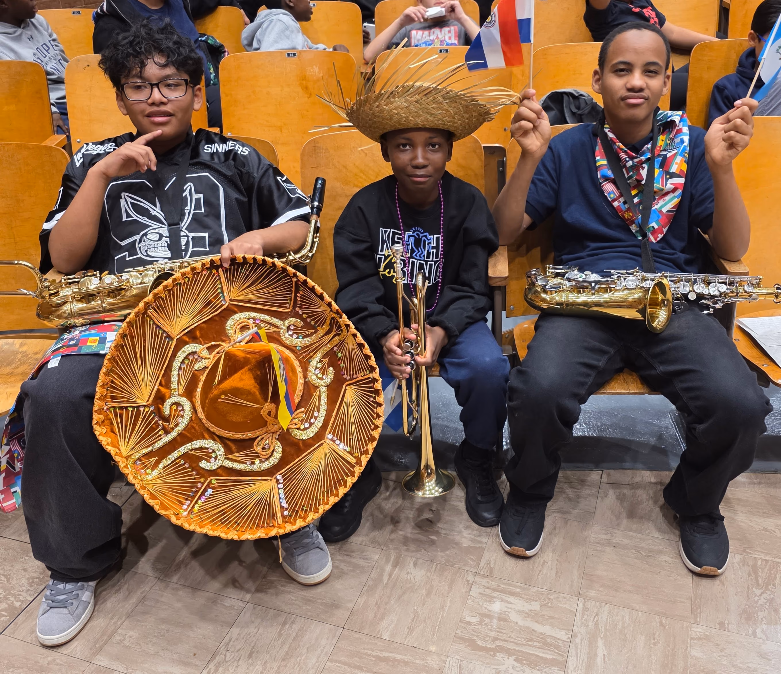 Three students holding instruments and cultural items at a school celebration