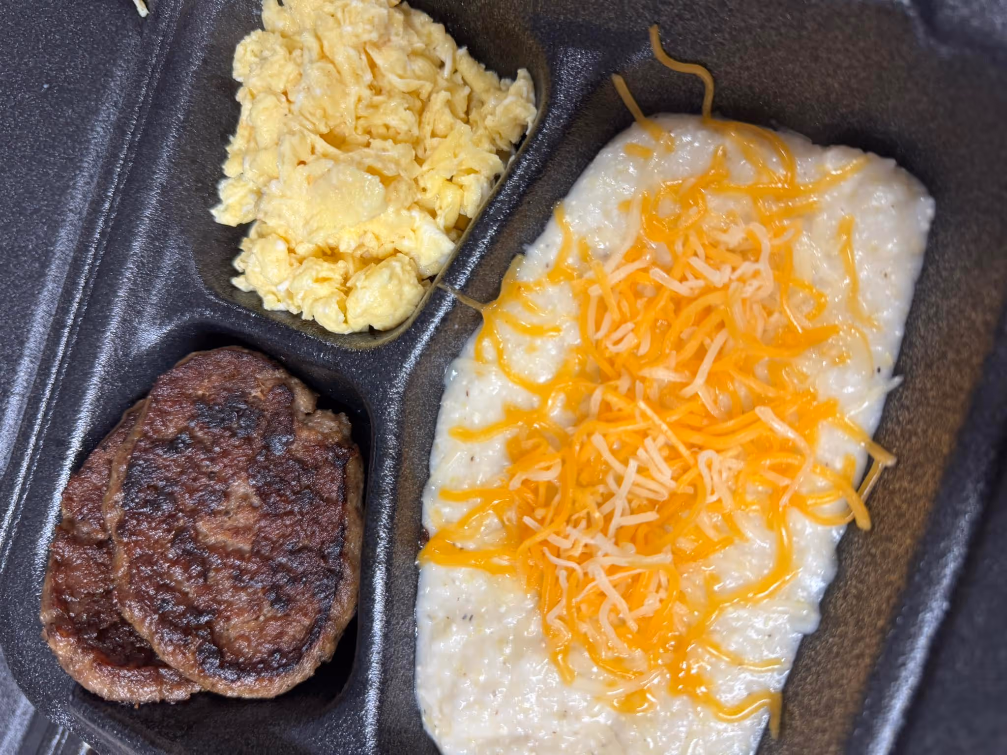A tray of food with a cheese and egg dish, meat, and grits.