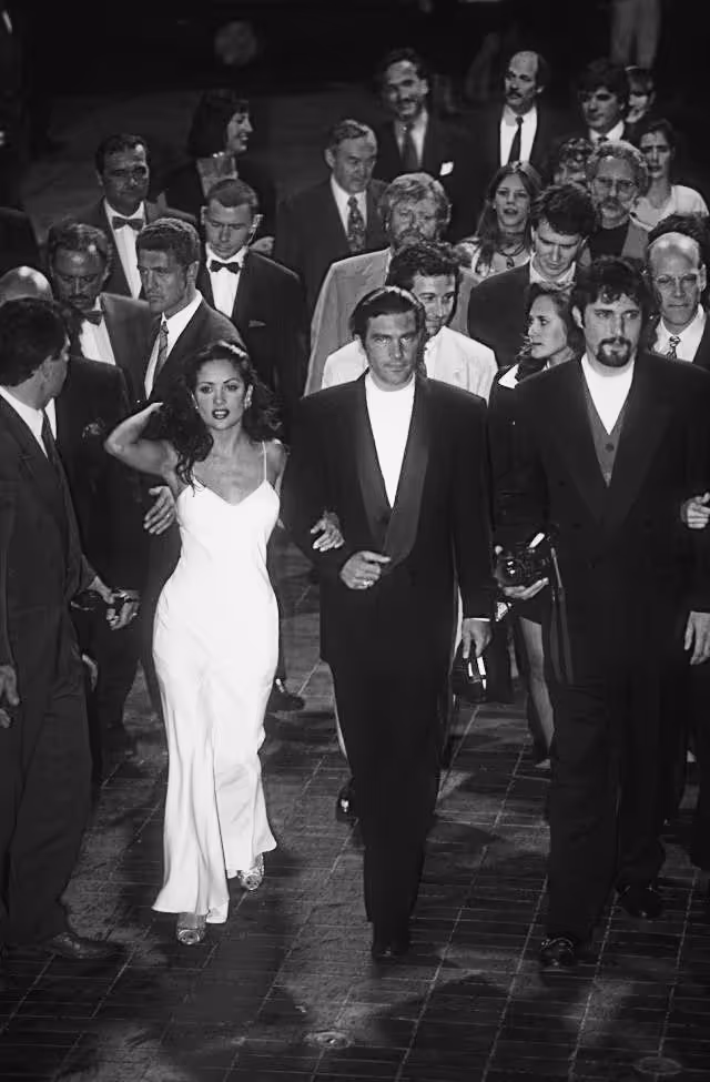 Black and white photo of a group of formally dressed people walking, with a woman in a white gown and men in tuxedos at the front.