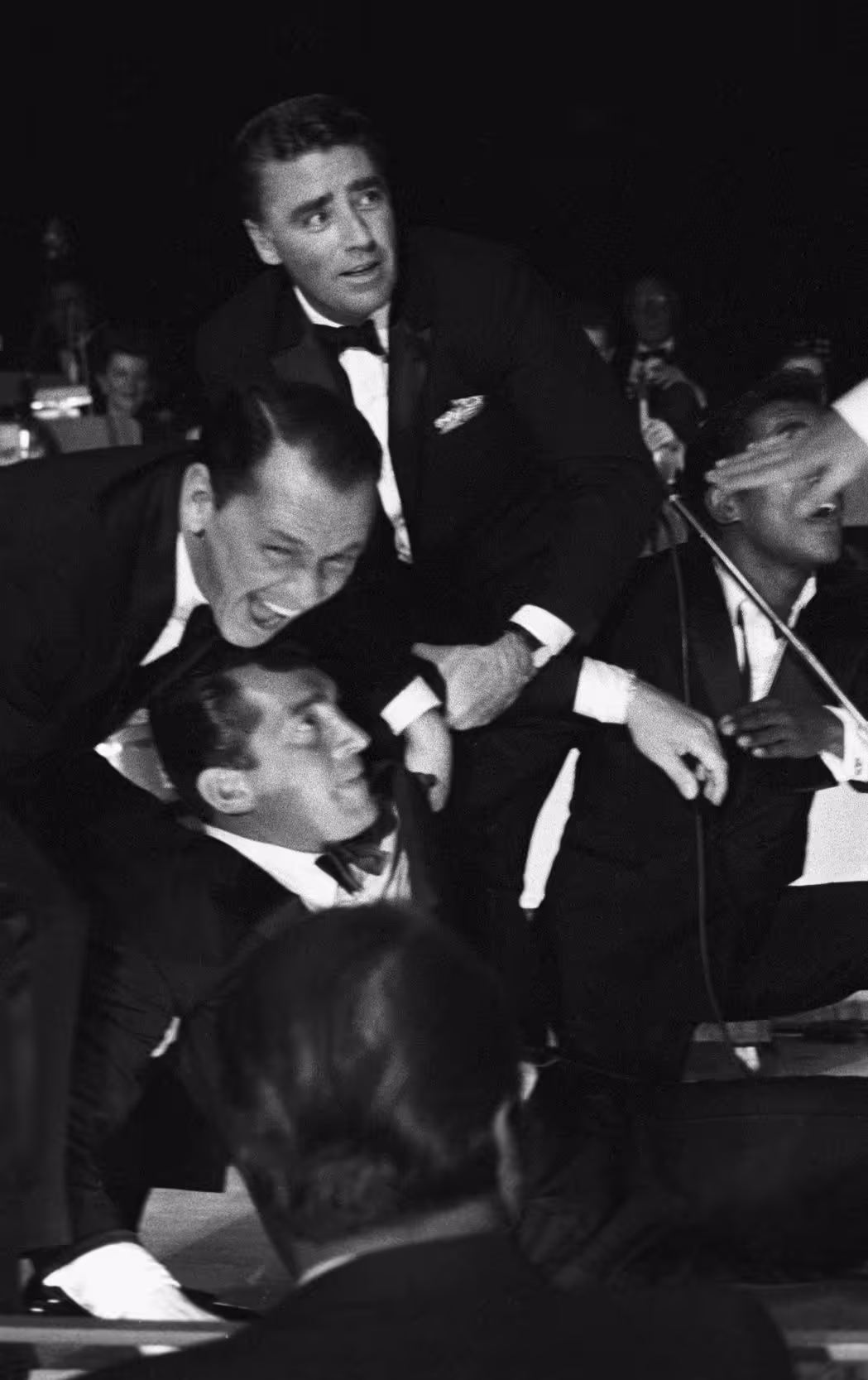 Black and white photo of men in tuxedos laughing and interacting at a formal event.