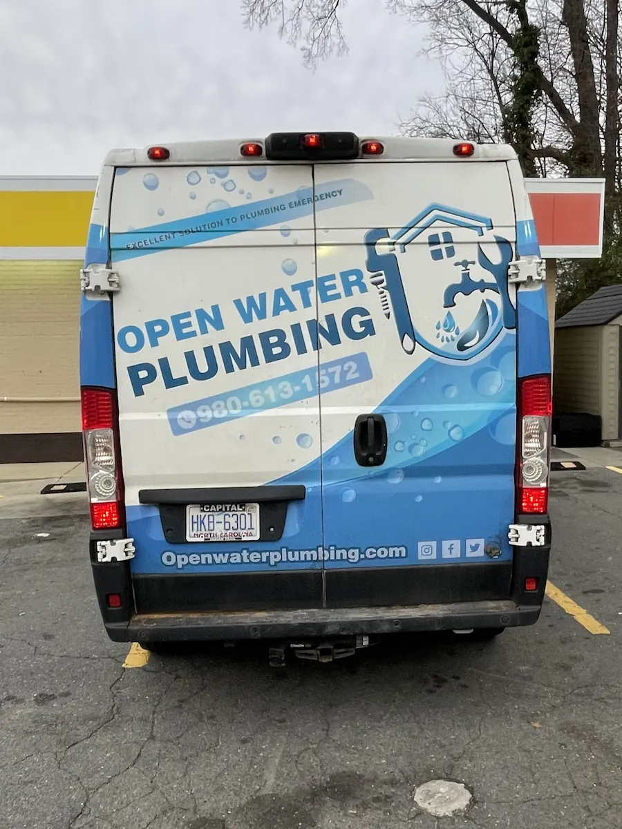 Rear view of a white and blue plumbing service van with Open Water Plumbing logo, contact number, and website.