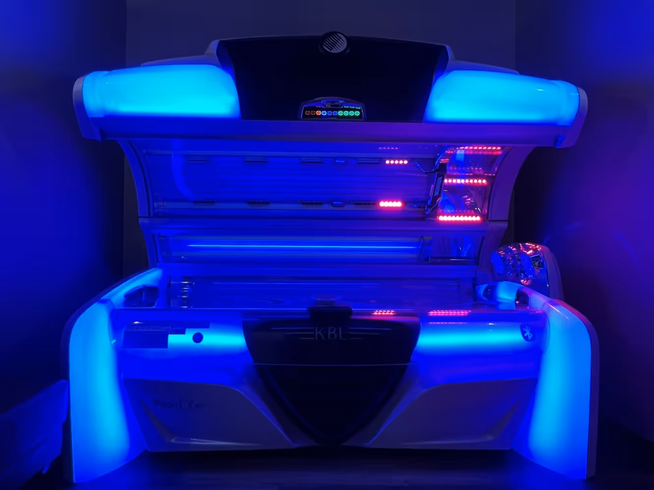 Open tanning bed illuminated with blue and pink lights in a dimly lit room.