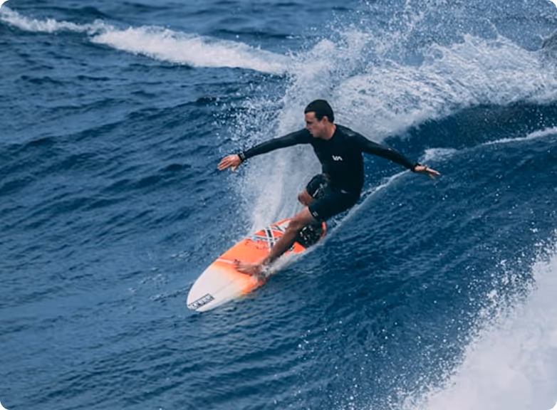 Surfer riding a wave on an orange and white surfboard in the ocean.