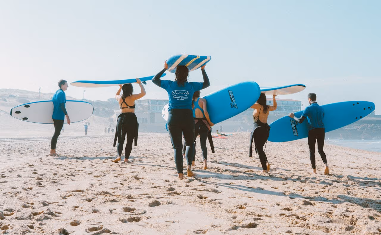Group of people carrying blue and white surfboards walking on a sandy beach toward the ocean.