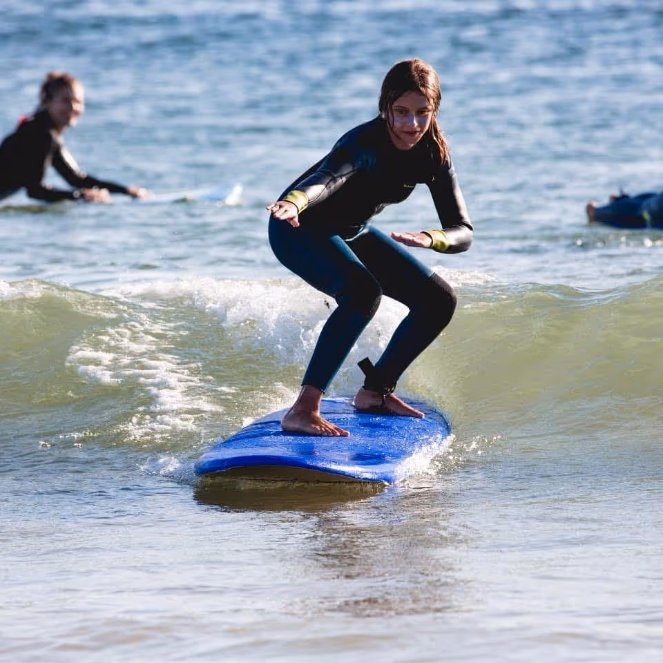 Young woman in a wetsuit surfing on a small wave on a blue surfboard.