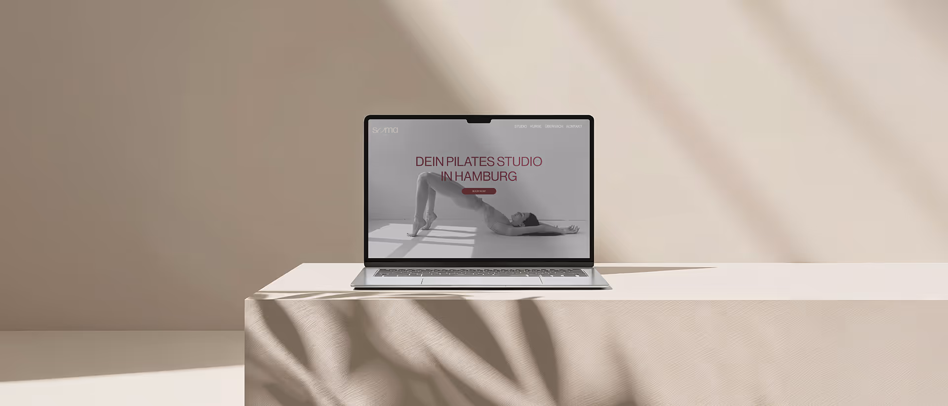 Laptop on a beige surface displaying a Pilates studio website with a woman performing a bridge pose.