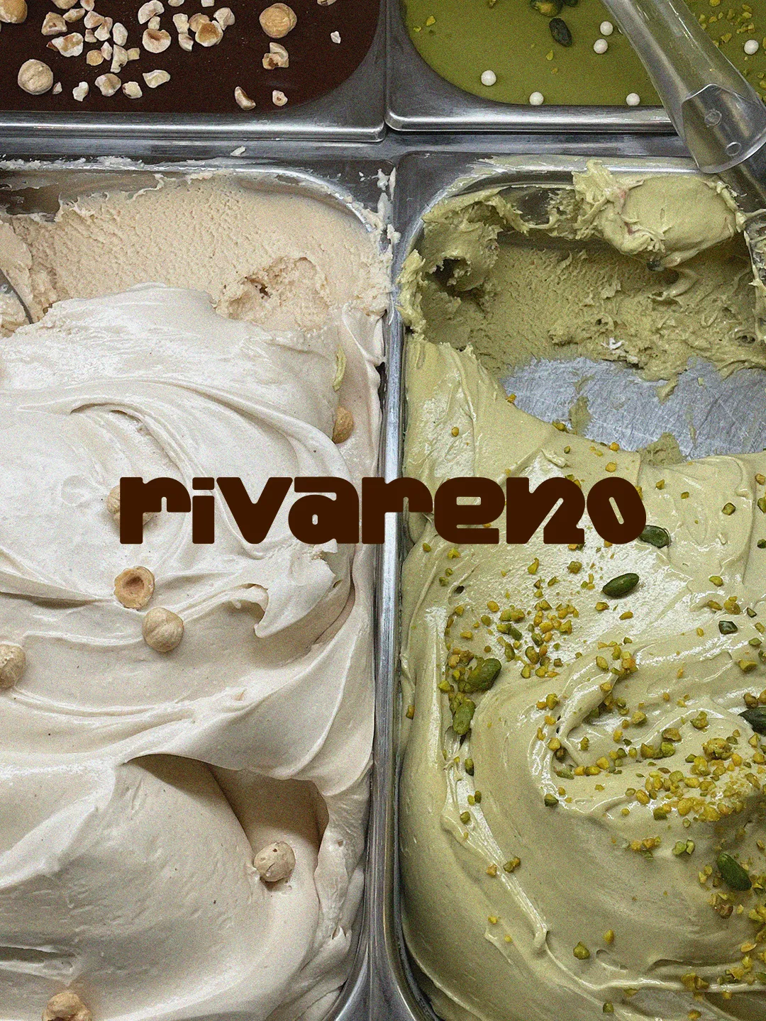 Verschiedene Sorten Eiscreme in Metallbehältern, darunter Pistazie mit Pistazienstückchen und Haselnuss mit Nüssen, mit braunem Schriftzug 'rivareno' in der Mitte.