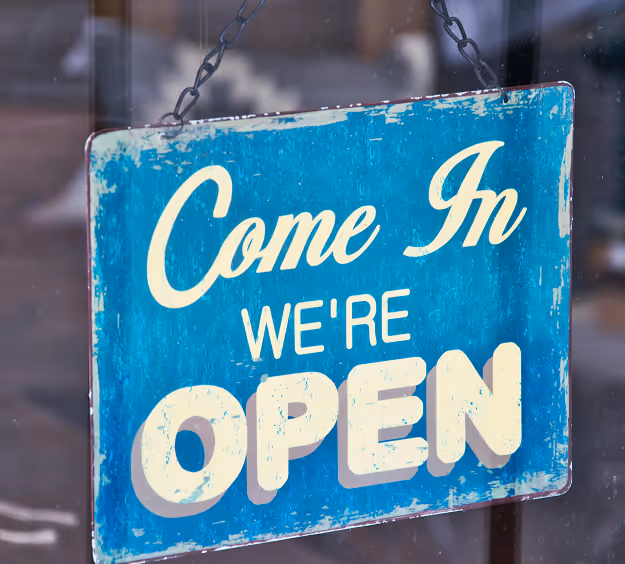 Blue vintage-style sign hanging on a door that reads 'Come In We're OPEN'.