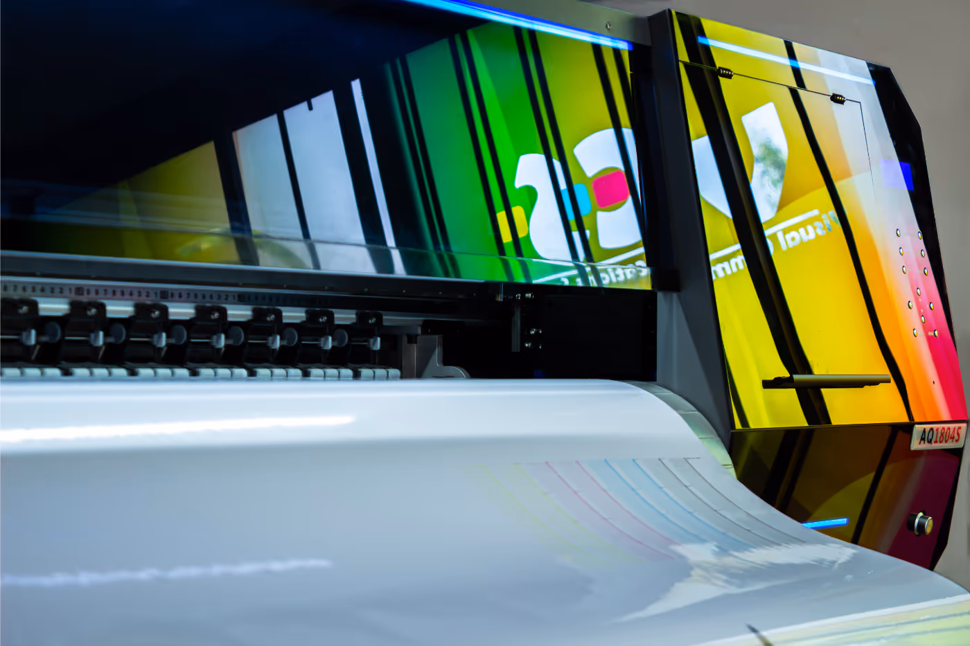 Large industrial printer producing a wide-format print with colorful design and visible printer head components.