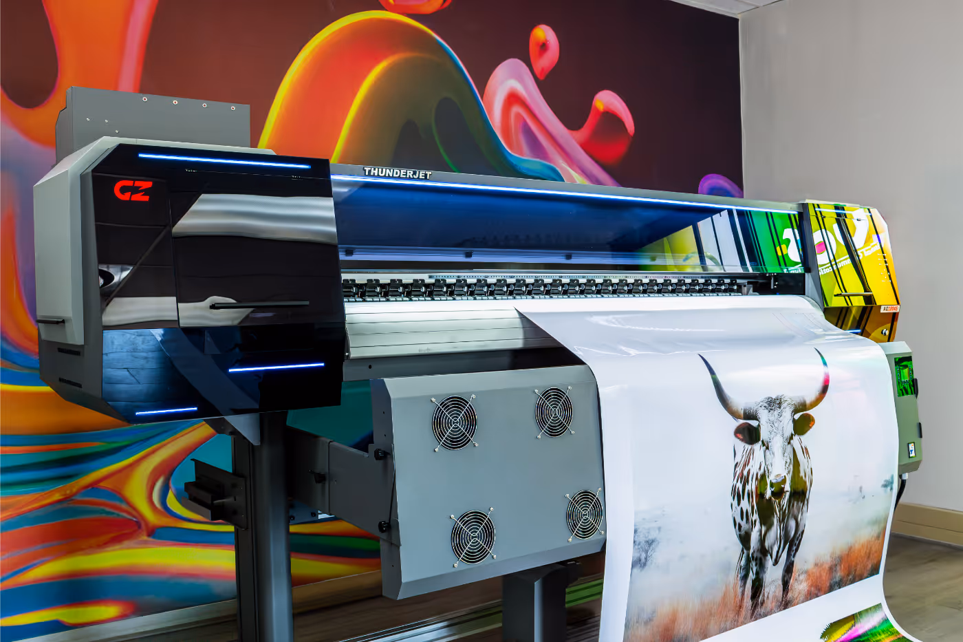 Large industrial printer producing a colorful print of a longhorn cattle in a room with a vibrant abstract mural on the wall.