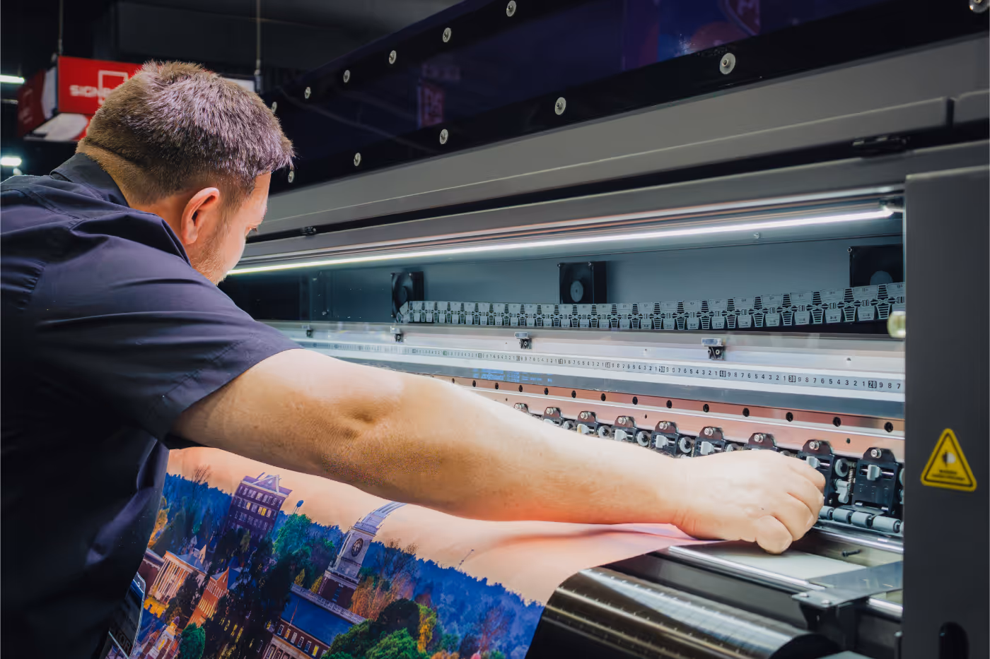 Man adjusting a large format printer producing a colorful cityscape print.