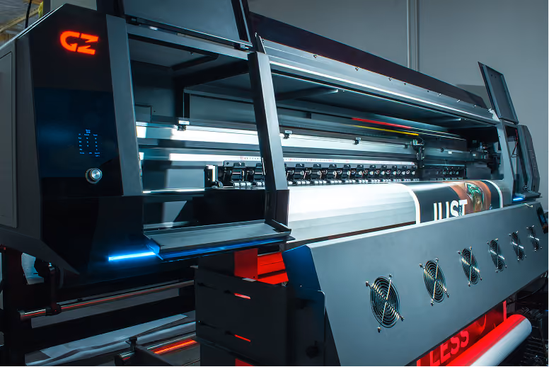 Large industrial digital printer producing a wide banner featuring part of the word JUST and an image, housed in a modern workspace with black and red accents.