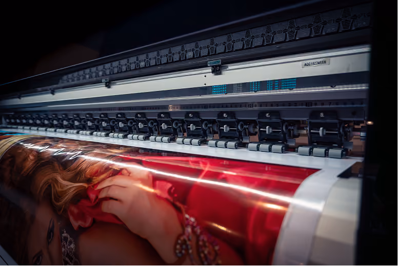 Large format printer producing a vibrant, glossy photo of a woman with red hair and red fabric, visible close to the printer head and rollers.