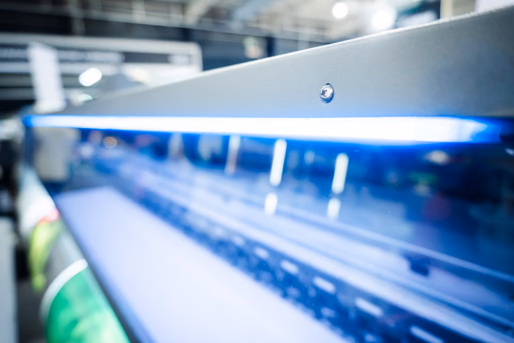 Close-up view of a blue UV light strip mounted on a metallic industrial machine panel inside a factory or workshop.