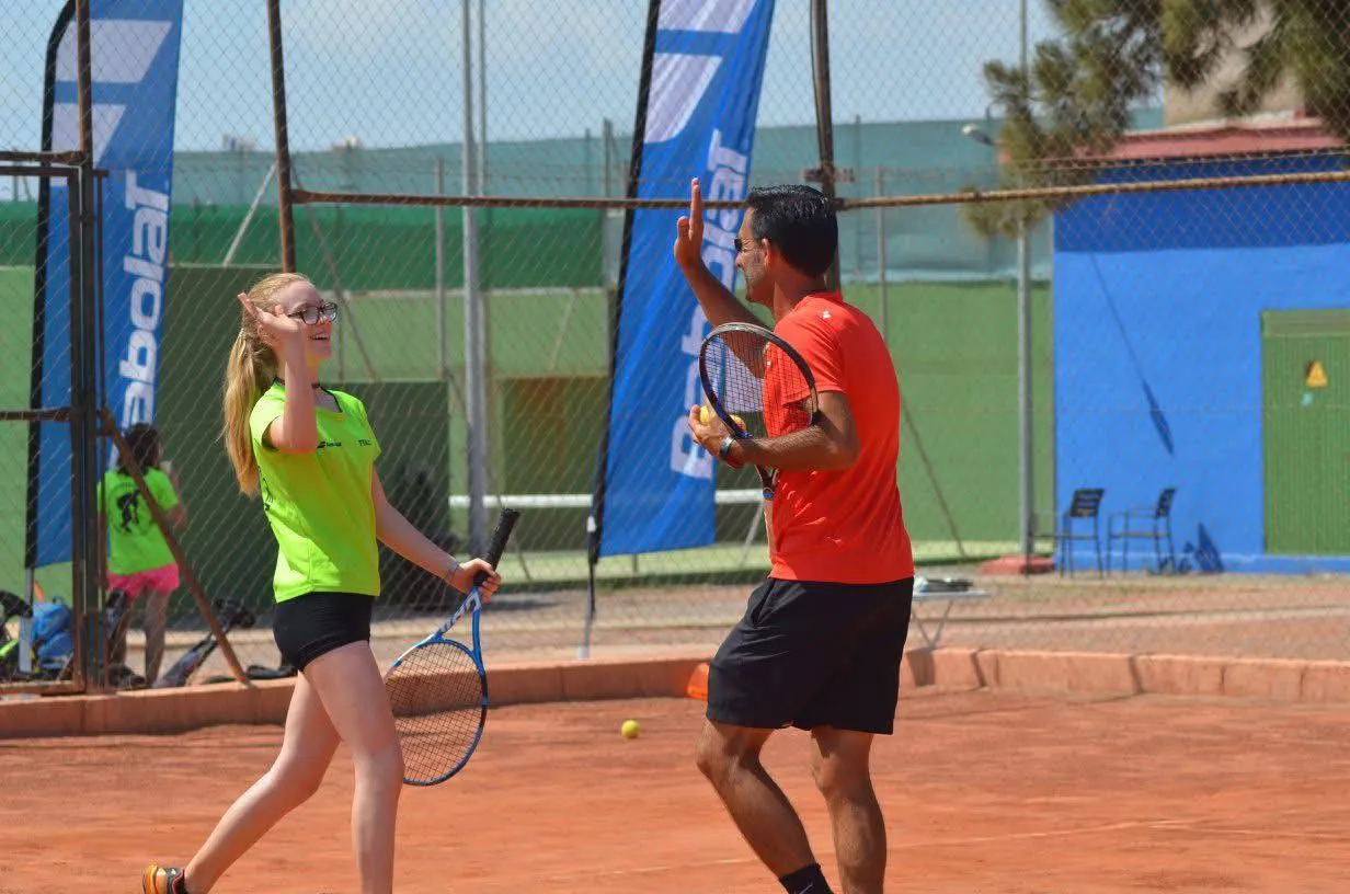 Two tennis players on a clay court giving a high-five, one wearing a lime green shirt and the other in an orange shirt.