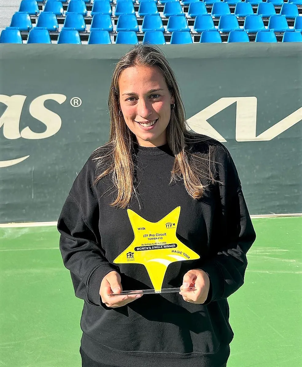Smiling woman holding a yellow star-shaped trophy for ITF Pro Circuit Women's Single Winner on a tennis court.