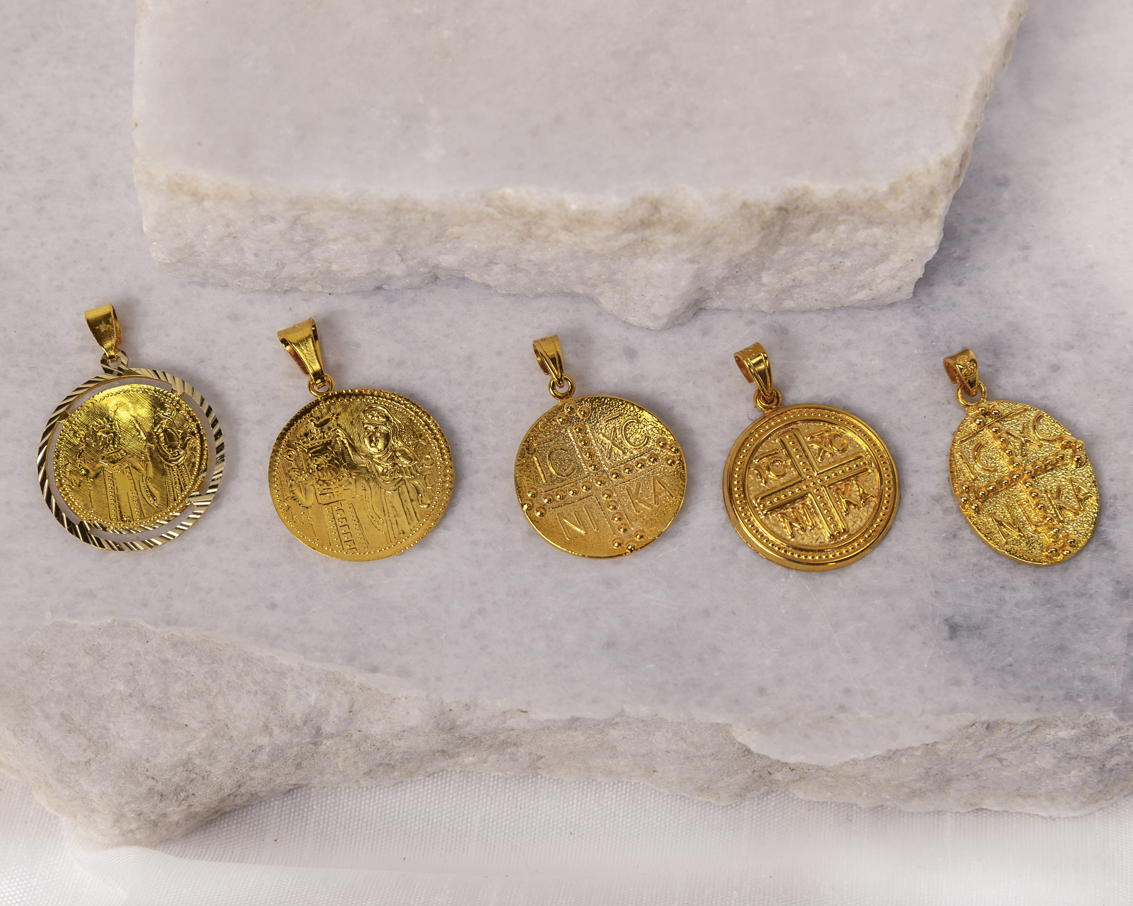 Five gold religious pendant coins with various embossed Byzantine-style designs and inscriptions, displayed on a marble slab.