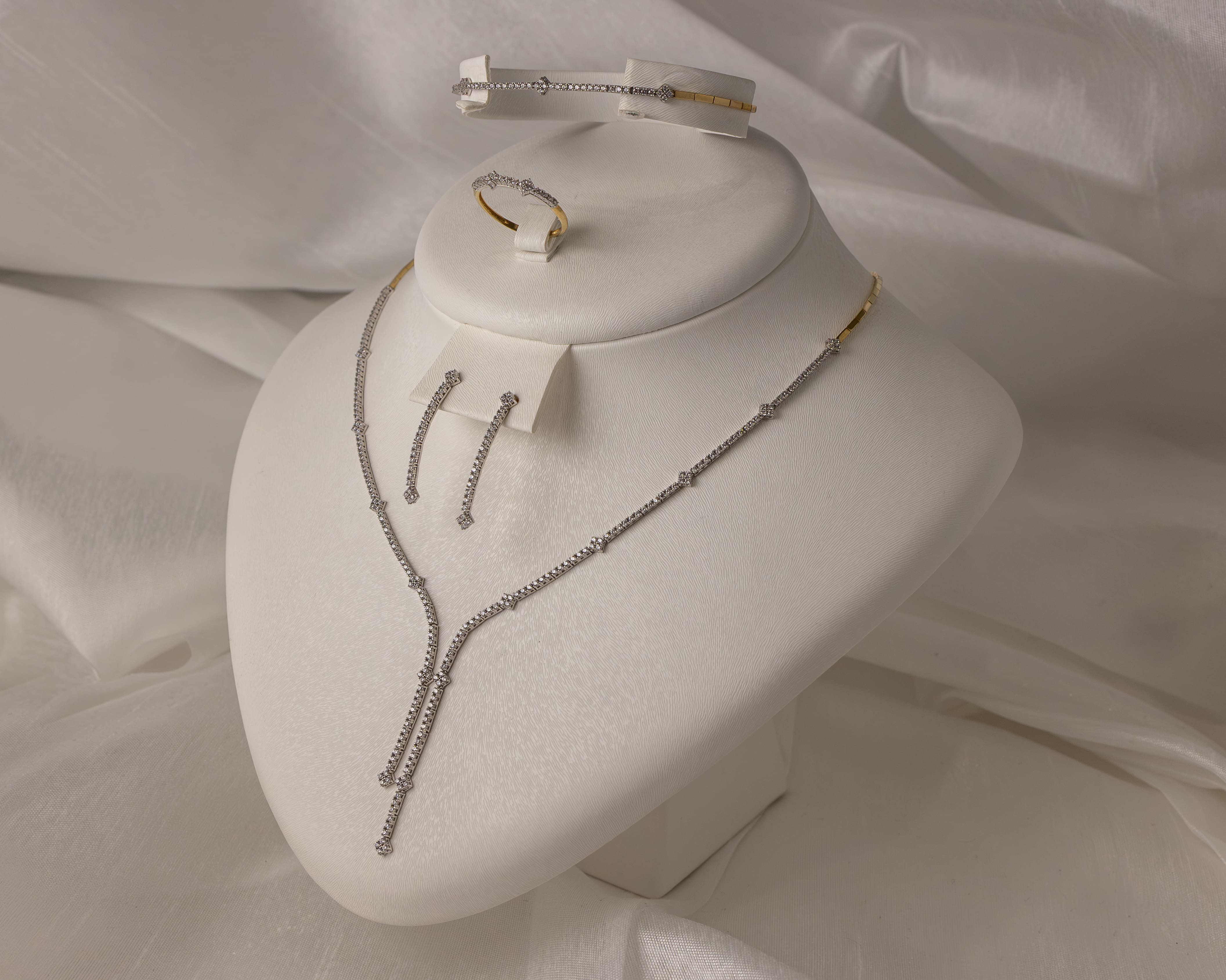 Jewelry set including a diamond necklace, matching earrings, a ring, and a bracelet displayed on a white stand.