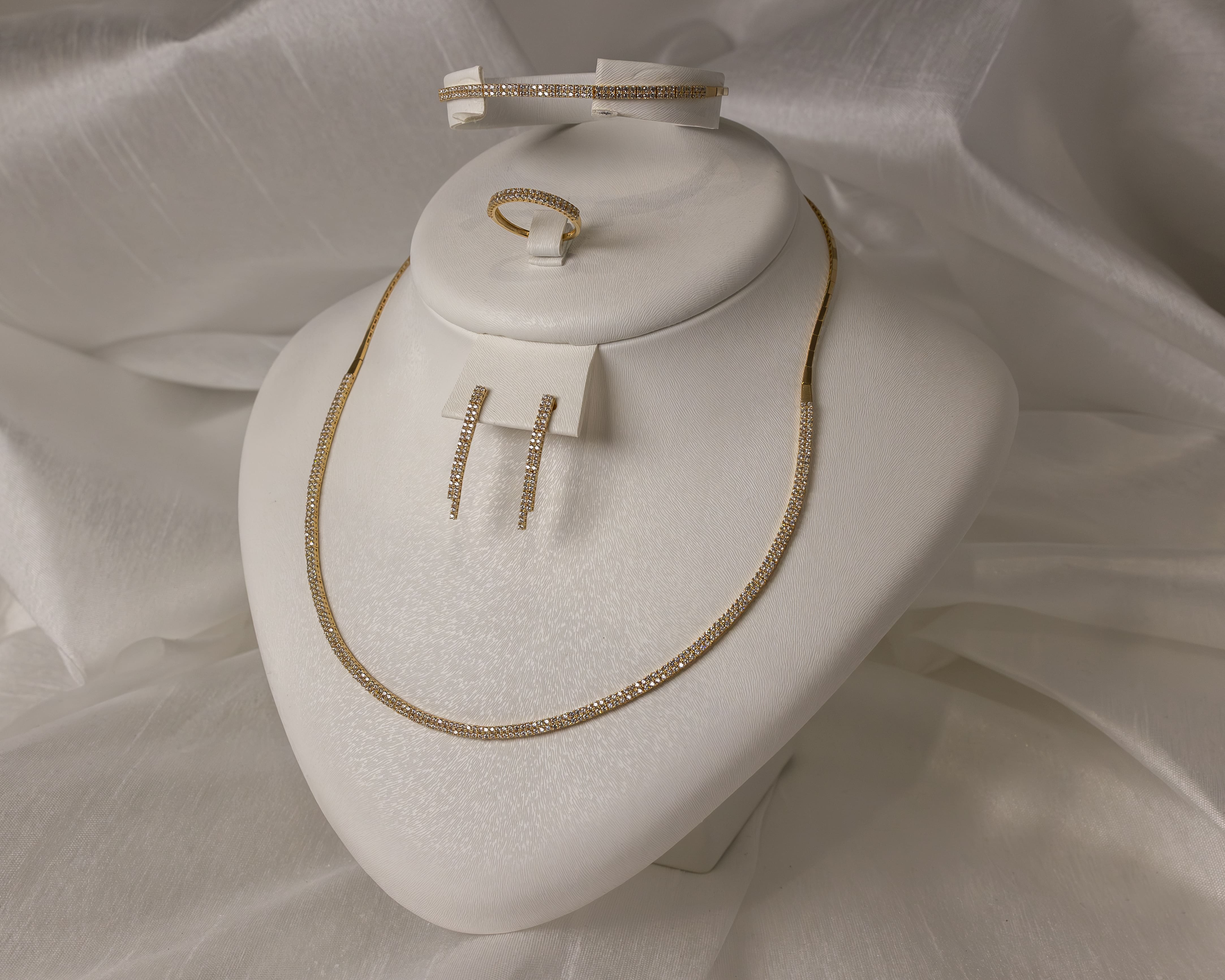 Gold jewelry set with a necklace, earrings, ring, and bracelet adorned with small diamonds displayed on a white stand.