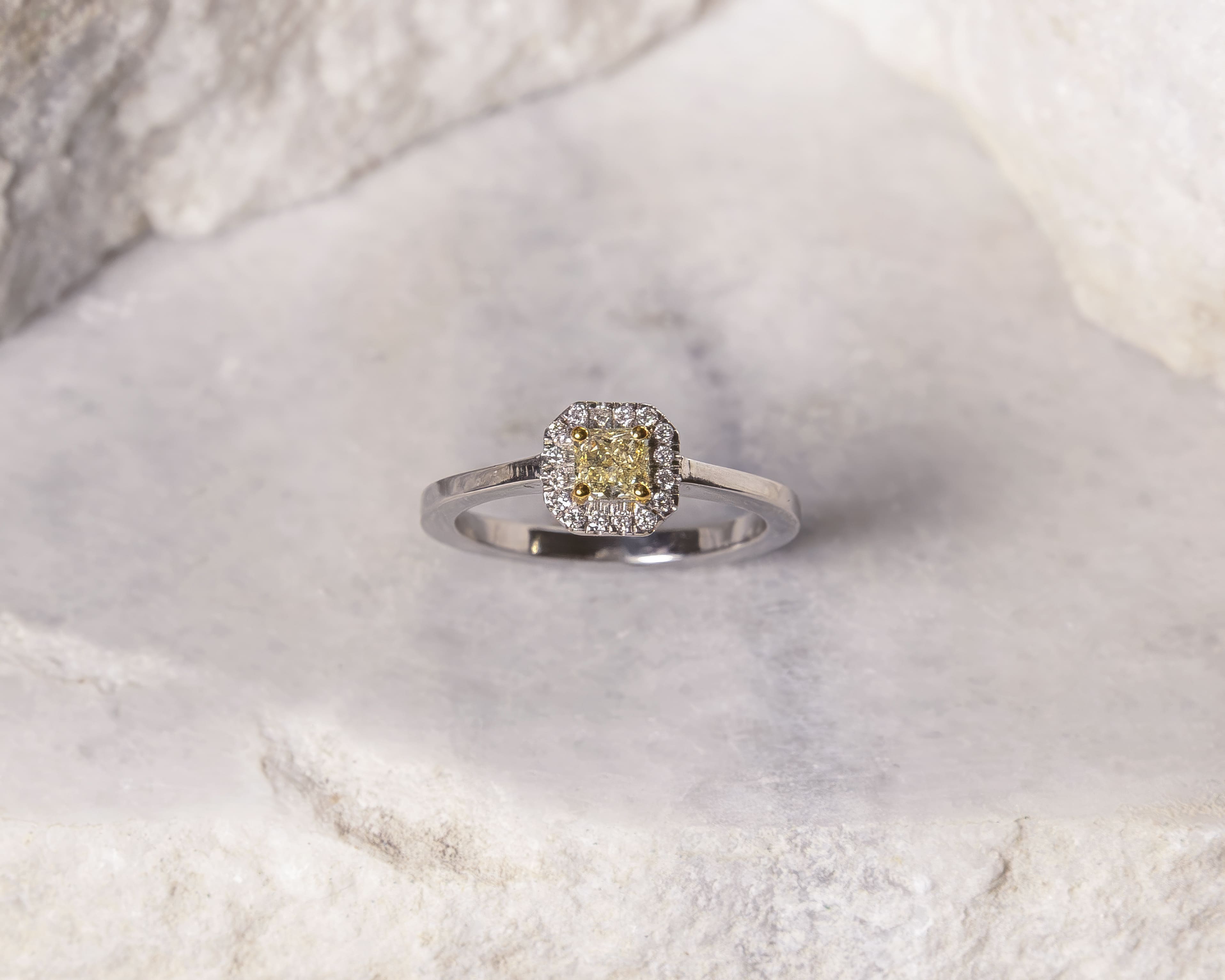Silver ring with a square yellow diamond center surrounded by smaller white diamonds on a light marble surface.