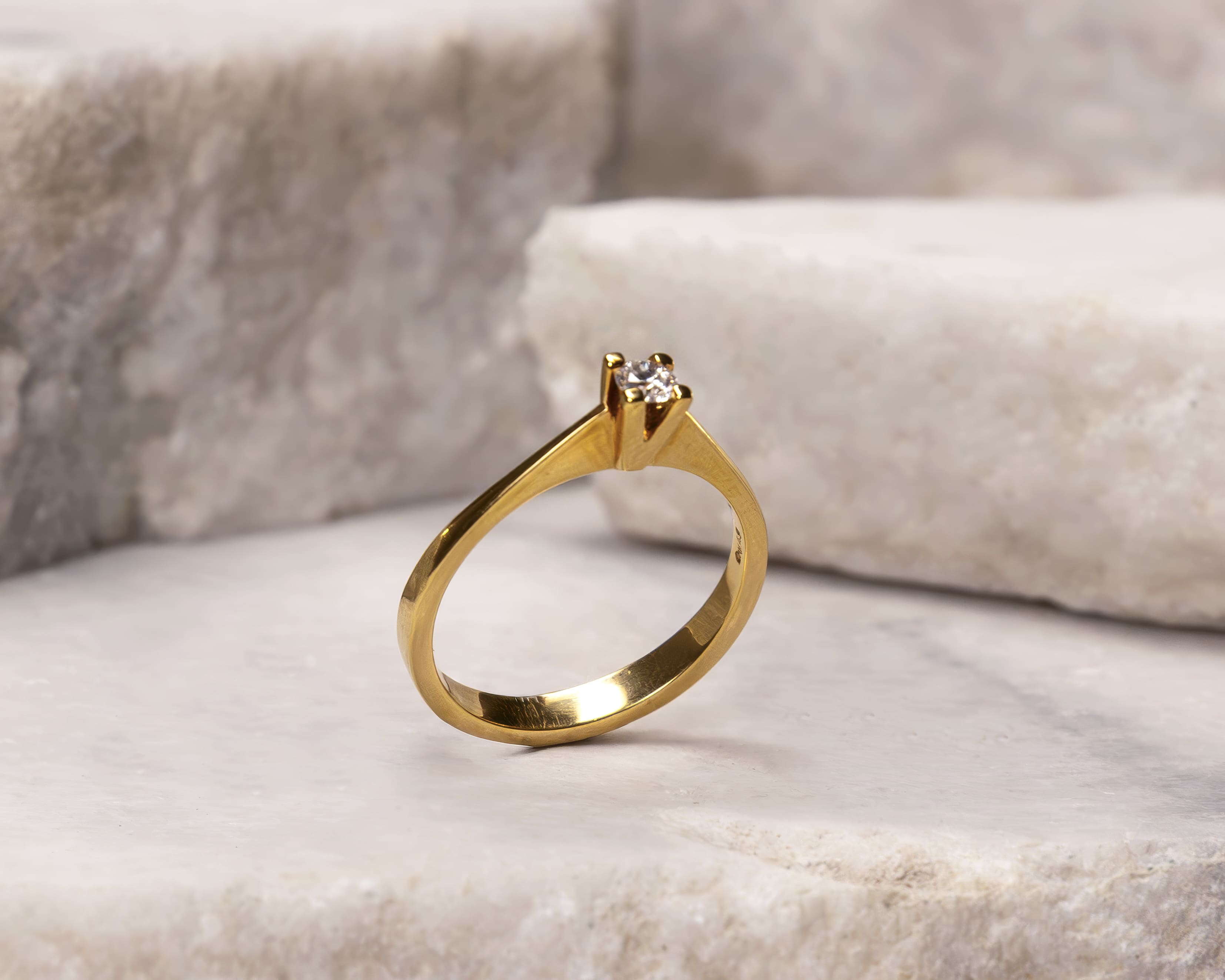 Gold solitaire ring with a single diamond on a light marble surface.